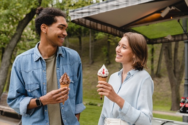 Happy young mixed-race couple eating ice-cream during date walking in city park in summer outdoors. Love and relationship concept.